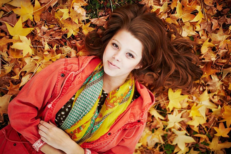 A young woman resting on a bed of fallen autumn leaves, representing the seasonal transition of deciduous trees.